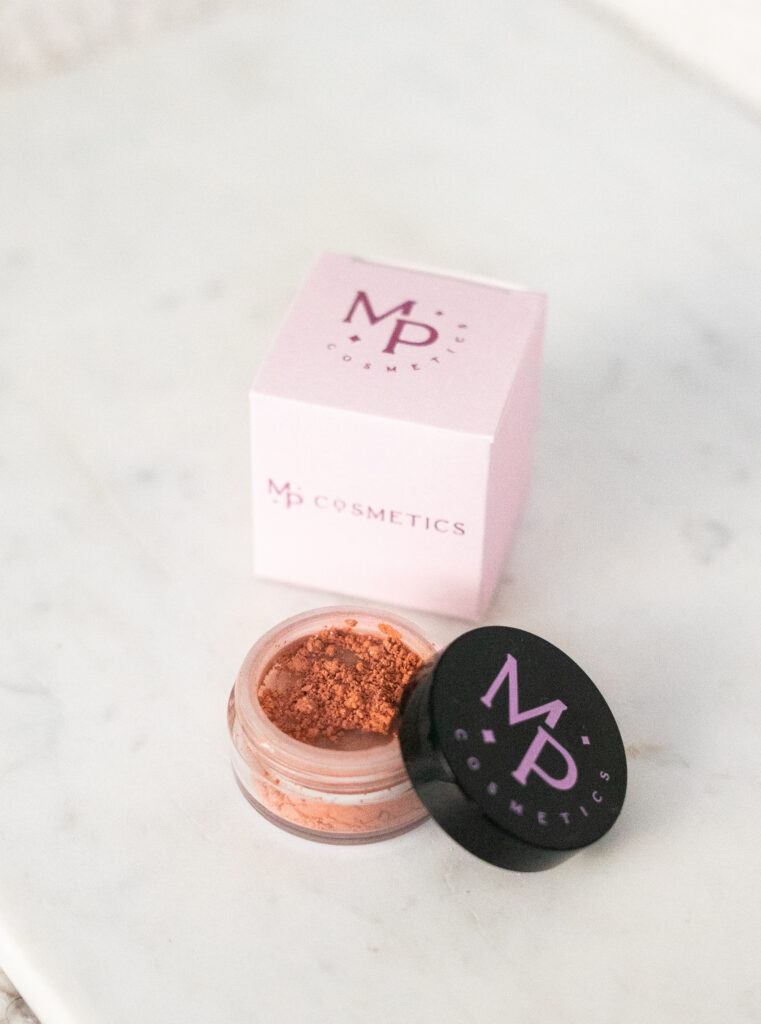 Oranžikas mineraalne põsepuna toonis "Õhtupuna" musta kaanega potsikus ja roosa karp.