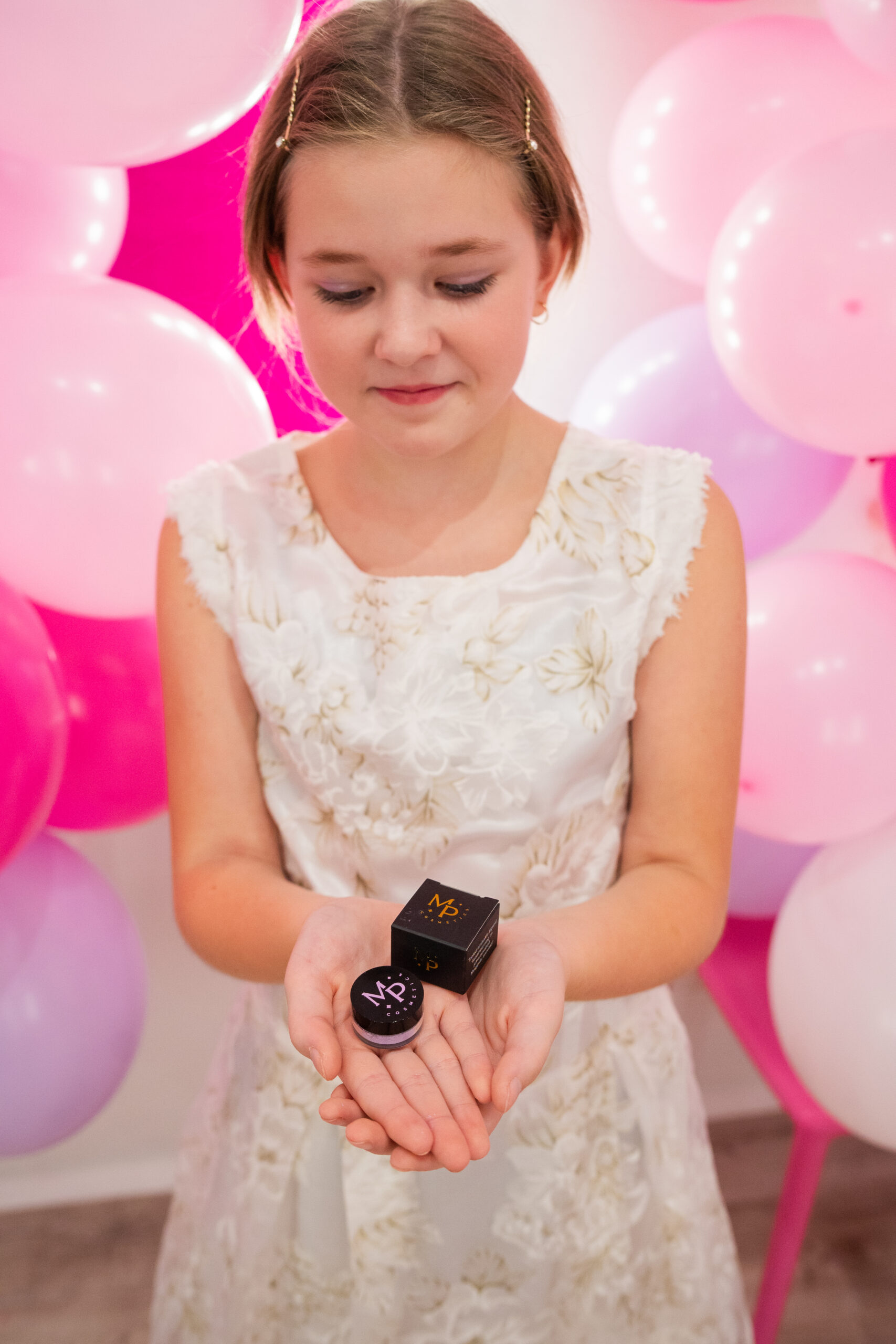 Lauvärv Lillepidu Väike tüdruk, kes on kasutanud mineraalset lillat pulberlauvärvi tooni "Lillepidu" oma silmameigis, hoiab lillat lauvärvi potsikut käes.